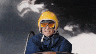 a man wearing a yellow helmet and goggles is riding a ski lift