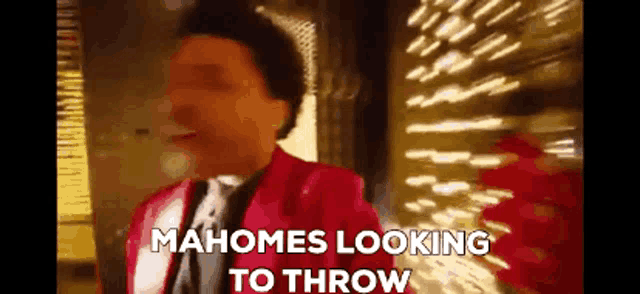 a man in a red jacket and tie is standing in front of a building and looking to throw something .