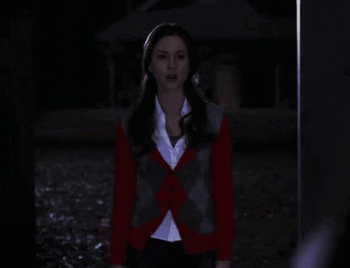 a woman in a red and gray cardigan stands in the dark