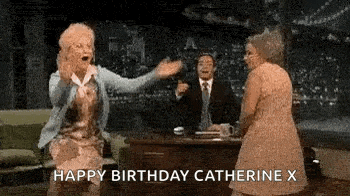 two older women are dancing in front of a man in a suit and tie while a man sits at a desk .