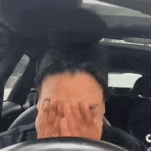 a woman covering her face in a car with the letter c on the steering wheel