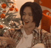 a man in a plaid shirt is smiling in front of a christmas tree .
