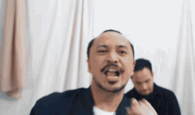 a man with a beard is screaming in front of another man