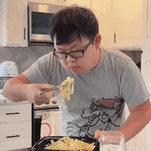 a man wearing glasses is eating noodles with a fork