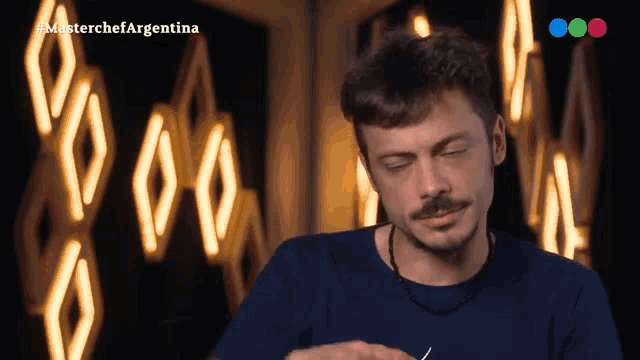 a man in a blue shirt is sitting in front of a screen that says " masterchef argentina "