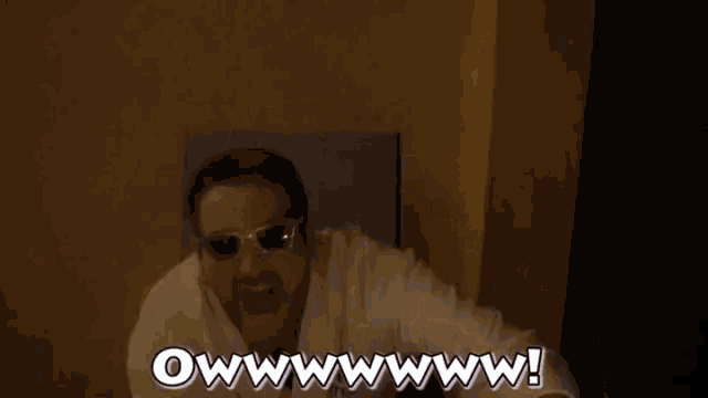 a man wearing sunglasses and a robe is sitting on a bed and making a funny face .