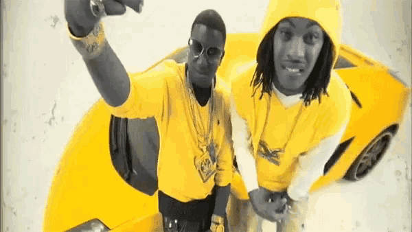 two men in yellow shirts are standing next to a yellow sports car