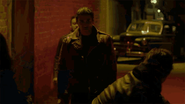 two men in leather jackets are walking down a dark alley