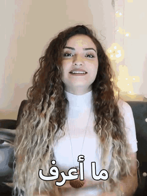 a woman with long curly hair is smiling and says " ma aref " in a foreign language