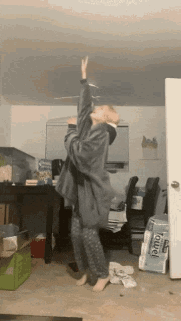 a woman is dancing in a room with a stack of towels in the background