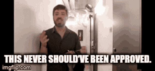 a man with a beard is standing in front of a wall and says this never should 've been approved .