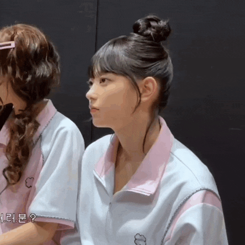 two girls are sitting next to each other and one of them has her hair in a bun