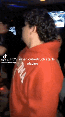 a man in a red hoodie is standing in a crowd with a caption that says " when cybertruck starts playing "