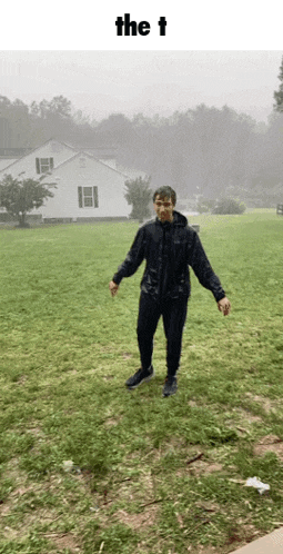 a man in a black jacket is standing in a grassy field with the word the t above him .