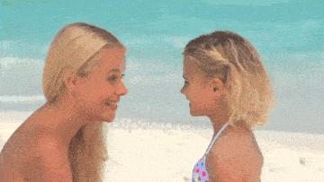 a woman and a little girl are looking at each other on a beach