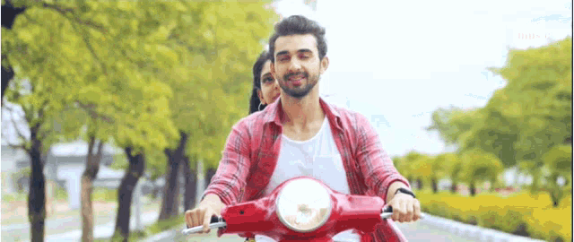 a man and woman are riding a red scooter down a road .