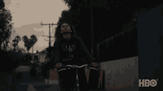 a person riding a bike down a street with hbo on the bottom right