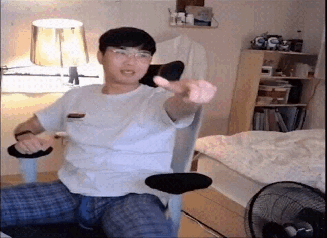 a man is sitting in a chair in a bedroom giving a thumbs up sign .