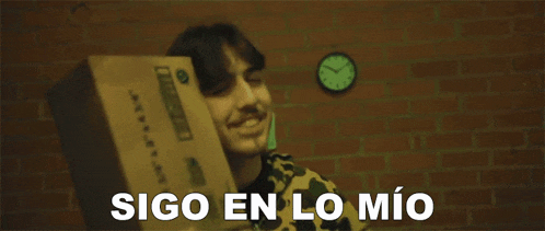 a man holding a cardboard box with the words sigo en lo mio written below him