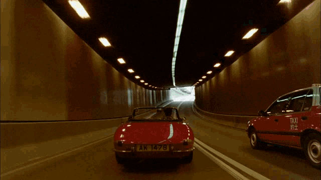 a man in a suit is driving a red car and holding a gun