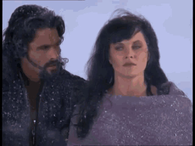 a man and a woman are standing in the snow looking at each other