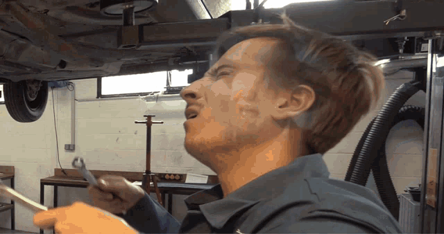 a man is holding a wrench in front of a car on a lift