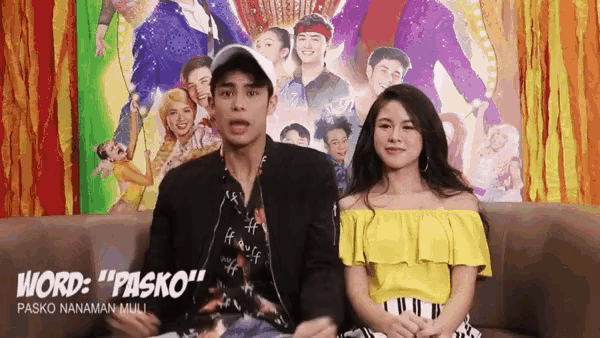a man and a woman are sitting on a couch in front of a poster for pasko