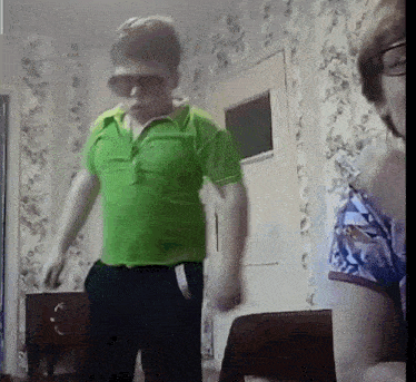 a man wearing sunglasses and a green shirt is dancing in a room .