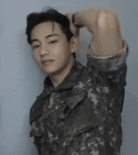 a young man in a military uniform is standing with his arms over his head .