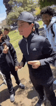 a group of young men are standing next to each other in a park . one of the men is wearing a baseball cap .