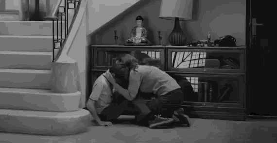 a black and white photo of a man and woman hugging each other in front of stairs .