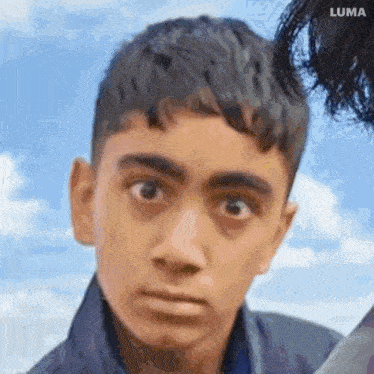 a close up of a young man 's face against a blue sky with clouds .