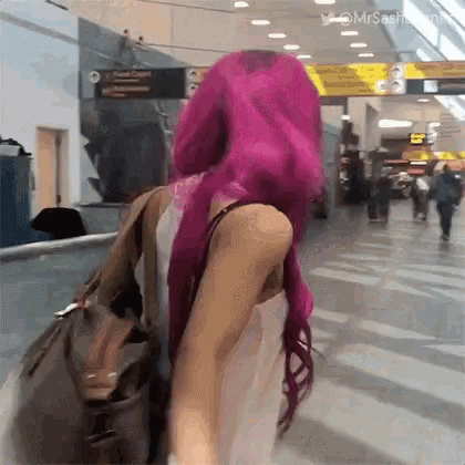 a woman with pink hair is walking down an escalator at an airport .