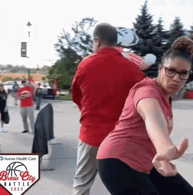 a woman in a red shirt is dancing in front of a sign that says brew city battle