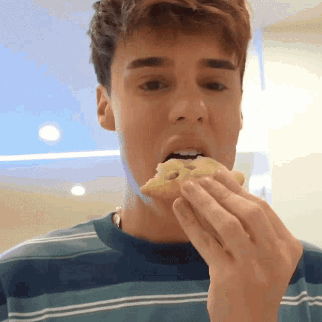 a young man in a striped shirt eating a cookie