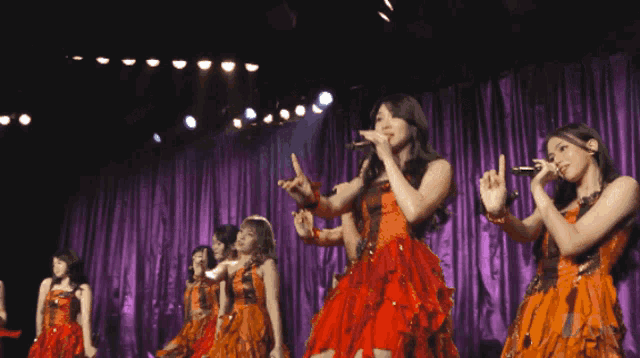 a group of women singing on a stage with purple curtains