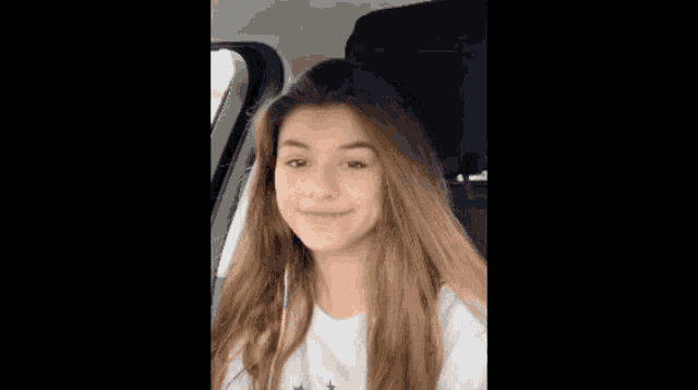a young girl with long hair is sitting in the back seat of a car .