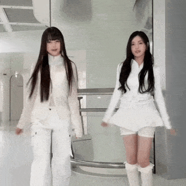 two girls in white clothes are dancing together in a room