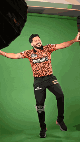 a man wearing a shirt that says dream11 is dancing in front of a green screen