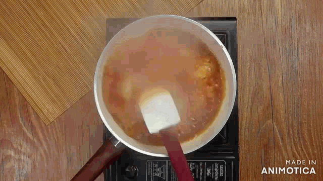 a pot of liquid is being stirred with a spatula on a stove .