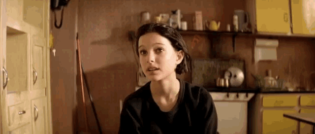 a young woman is sitting in a kitchen with a mop and a telephone .