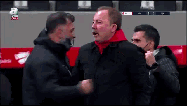 a man in a black jacket is talking to another man in a red hoodie while wearing a mask .
