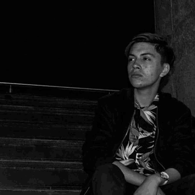 a young man is sitting on a set of stairs wearing a floral shirt and a black jacket .