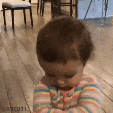 a baby is sitting on a wooden floor with his arms crossed and his eyes closed .