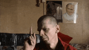 a man in a red shirt holds up his finger in front of a picture of pope john paul ii and another picture