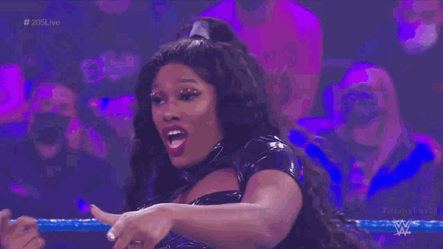 a woman in a black dress is standing in front of a crowd in a wrestling ring .