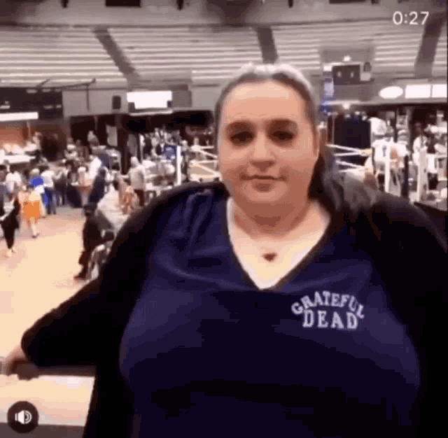 a woman wearing a blue grateful dead shirt is standing in a gym .