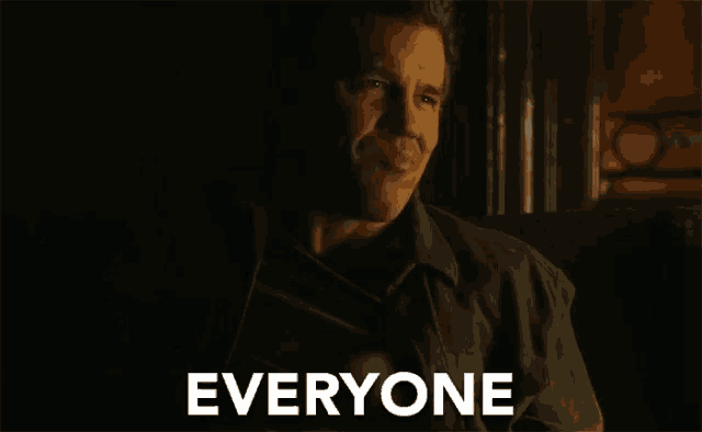 a man is sitting in a dark room and the word everyone is on the screen behind him