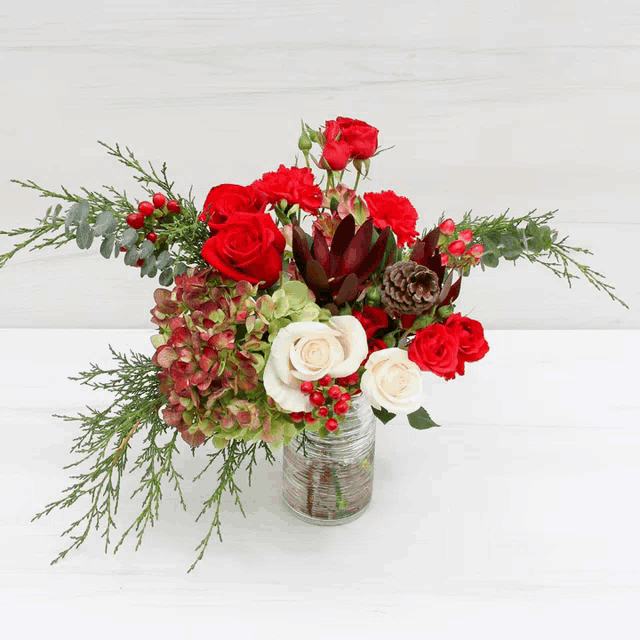a vase filled with red and white flowers and berries