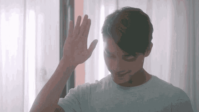 a young man waves his hand in front of his face
